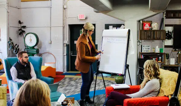 Image of a woman at an easel presenting to colleagues. It's important to start with an assessment for custom software.